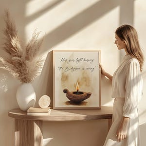 May include: A framed print featuring a watercolor illustration of an oil lamp with a lit flame. The text "Keep your light burning. The Bridegroom is coming" is written above the lamp. The artwork is displayed on a wooden table.