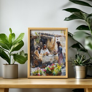 May include: A framed watercolor painting depicting a scene of Jesus with two women. The painting is set in a rustic outdoor setting with a table and flowers. The painting is framed in a light wood frame.