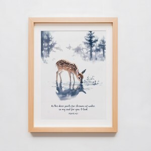 Könnte beinhalten: Ein gerahmter Druck mit einer Aquarell-Illustration eines Rehs, das an einem Bach im Wald trinkt. Der Druck enthält den Text "Wie der Hirsch nach Wasserbächen lechzt, so dürstet meine Seele nach dir, Gott. Psalm 42,1"