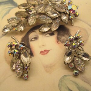 May include: A vintage jewelry set featuring a brooch and matching earrings. The set has a silver-tone metal base with clear, faceted crystal leaves and iridescent accents. The brooch is a spray of leaves, and the earrings are clusters of leaves.