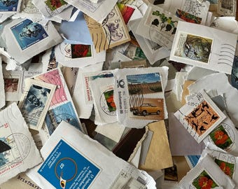 May include: A scattered assortment of vintage postage stamps and envelopes. The stamps display diverse designs, including portraits, landscapes, and floral patterns. The envelopes have torn edges, indicating they are part of a collection or display.