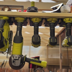 Peut inclure: Un ensemble de six outils électriques suspendus à un support mural. Les outils sont tous jaunes et noirs et comprennent une perceuse, une scie, une ponceuse et une meuleuse. Les outils sont tous suspendus à des crochets sur le support.