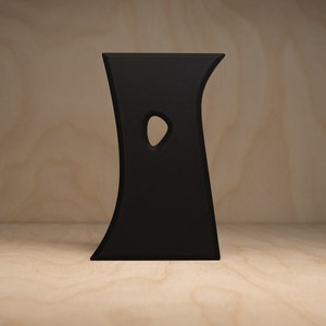 May include: A black, abstract, free-standing sculpture with a curved, organic shape and a single cutout in the center.