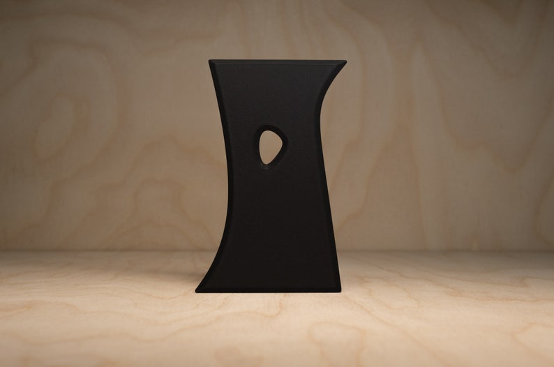 May include: A black, abstract, free-standing sculpture with a curved, organic shape and a single cutout in the center.