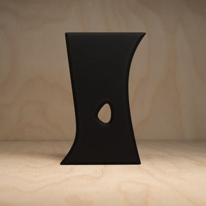 May include: A black, abstract, ceramic sculpture with a hole in the middle. The sculpture is standing on a light brown wooden surface.