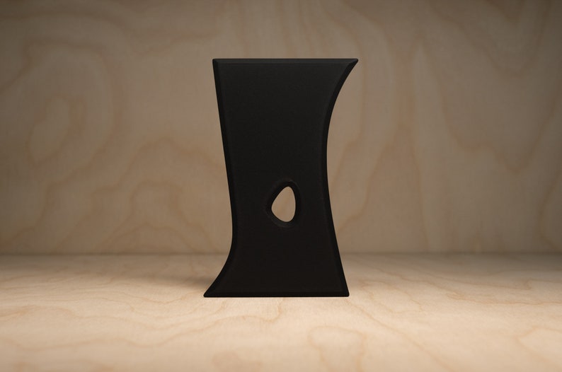 May include: A black, abstract, ceramic sculpture with a hole in the middle. The sculpture is standing on a light brown wooden surface.