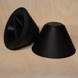May include: Two black foam cones, one with a cut-out section, on a light wood surface.