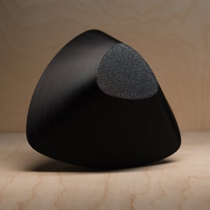 May include: A black triangular ceramic bowl with a textured, circular, gray patch on the top.