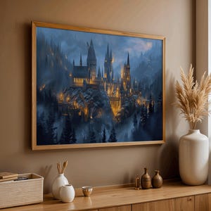 May include: A framed print of a castle with multiple towers, set against a misty, mountainous backdrop. The castle is illuminated with warm, golden light, contrasting with the cool blues and greens of the surrounding landscape. The frame is made of light-colored wood.