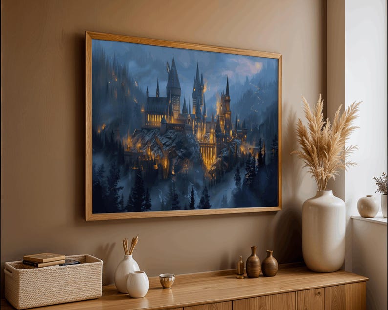 May include: A framed print of a castle with multiple towers, set against a misty, mountainous backdrop. The castle is illuminated with warm, golden light, contrasting with the cool blues and greens of the surrounding landscape. The frame is made of light-colored wood.
