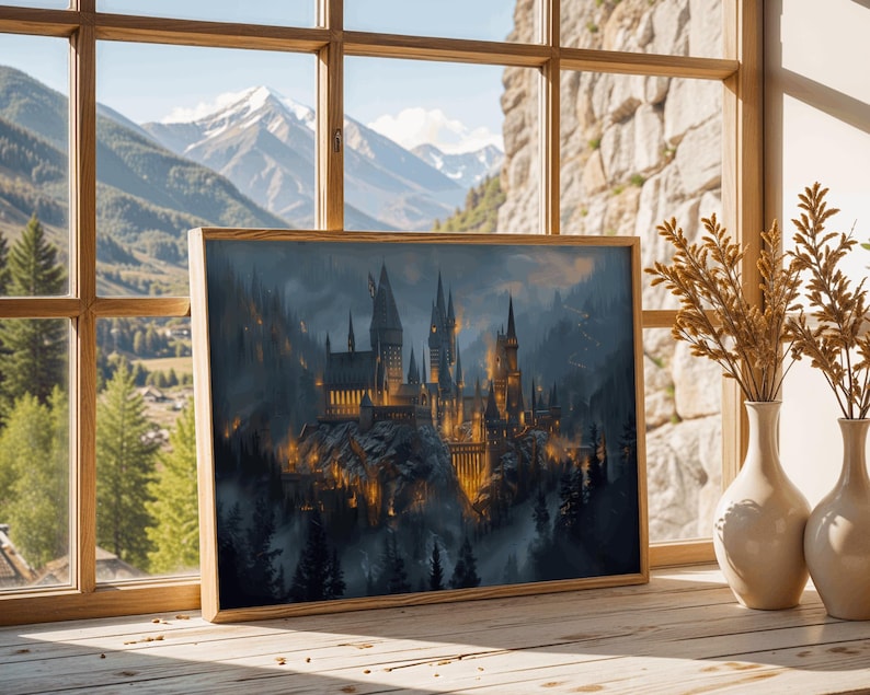 May include: A framed print of a castle on a mountain, with a wooden frame. The artwork depicts a detailed, illuminated castle with multiple towers, set against a backdrop of a misty forest and mountains. The print is displayed on a wooden surface near a window.