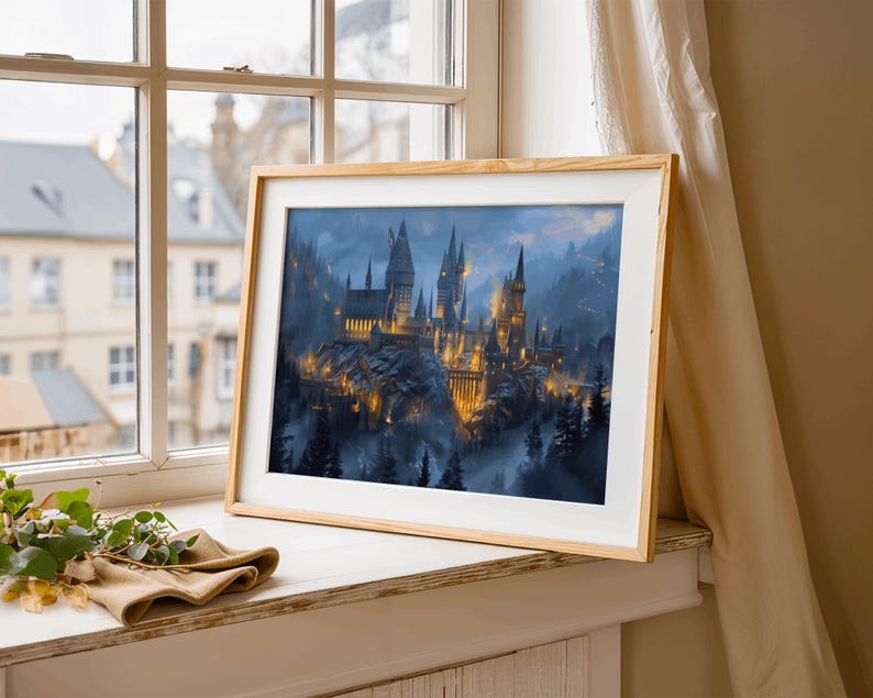 May include: A framed print of a castle with illuminated towers and spires, set against a misty, mountainous backdrop. The artwork is in a light wood frame, resting on a windowsill with a neutral-toned cloth and greenery.