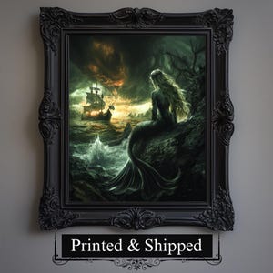 Puede incluir: Una obra de arte enmarcada representa a una sirena en una costa rocosa, mirando un barco en un mar tormentoso. La obra de arte está en un marco negro adornado. La sirena tiene pelo largo y rubio y una cola verde. El mar está turbulento con olas rompiendo.
