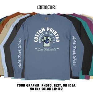 May include: A blue long-sleeve t-shirt with a white graphic of a t-shirt with a globe design. The text "Custom Printed Comfort Colors 1717" is in a white arc above the graphic. The text "Zen Threads" is below the graphic. The shirt has a white text "Add Text Here" on the left sleeve.