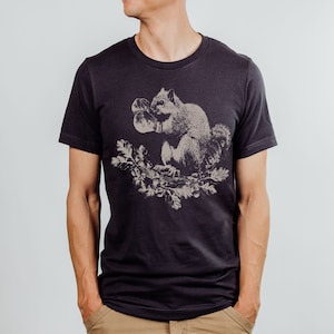 May include: A dark grey t-shirt with a graphic print of a squirrel wearing boxing gloves. The squirrel is sitting on a branch with leaves and acorns.