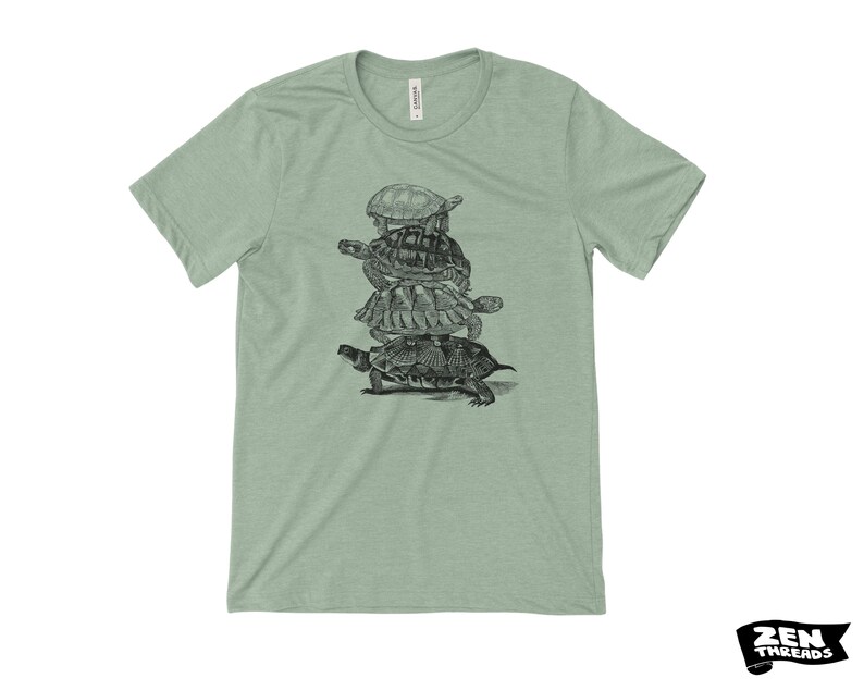 May include: A pale green t-shirt with a black and white drawing of five turtles piled up. The shirt has a crew neck and short sleeves. The brand logo "ZEN THREADS" is in the bottom right corner.