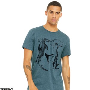 May include: A teal blue t-shirt with a black and white graphic print of a hammerhead shark, a shark tooth, and a stingray.