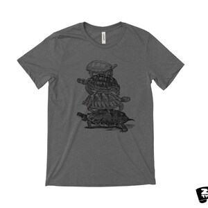 May include: Charcoal grey t-shirt with a black and white graphic of turtles piled up. The shirt has a crew neck and short sleeves. The brand logo "ZEN THREADS" is in the bottom right corner.