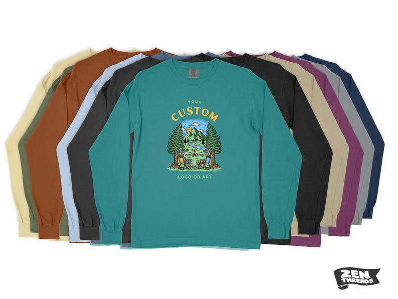 Pode incluir: Um conjunto de dez t-shirts de manga comprida em v&aacute;rias cores, com uma t-shirt turquesa com um design de logotipo personalizado de uma cena de acampamento com o texto "Your Custom Logo or Art".