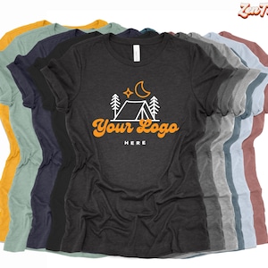 May include: A stack of t-shirts in various colors, including heather gray, mustard yellow, teal, and navy blue. The heather gray t-shirt features a white graphic of a tent, trees, a moon, and stars with the text "Your Logo Here" in orange.