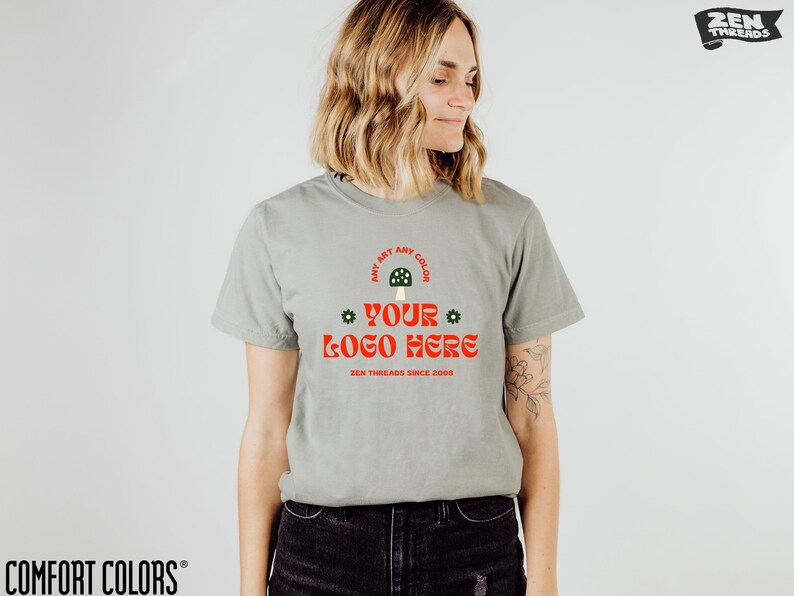 May include: A light green t-shirt with a mushroom graphic and the text "ANY ART ANY COLOR * YOUR LOGO HERE * ZEN THREADS SINCE 2000".