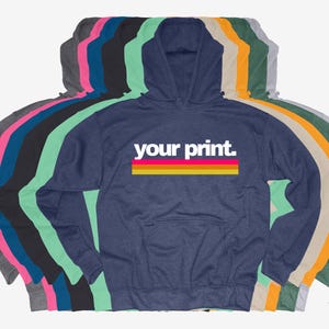 May include: A navy blue hooded sweatshirt with a white stripe and the text "your print" in white letters with a pink and yellow stripe underneath. The sweatshirt is shown with a variety of other colours.