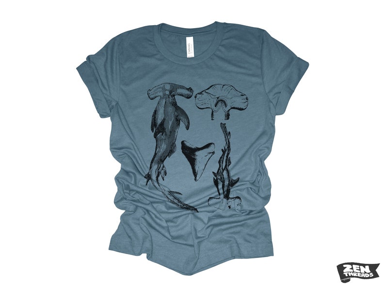 May include: A blue t-shirt with a black and white graphic print of a hammerhead shark, a shark tooth, and a shark fin.