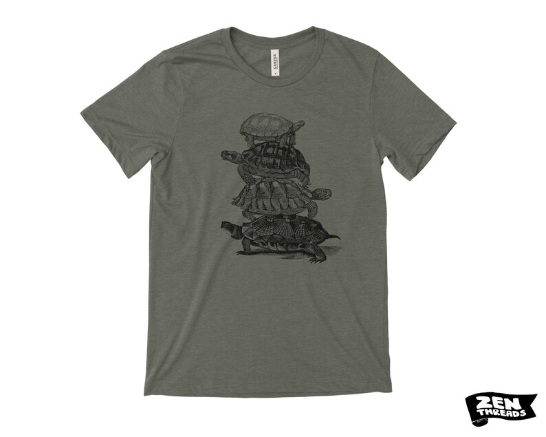 May include: A heather green t-shirt with a black and white illustration of a stack of turtles. The design shows three turtles stacked on top of each other. The shirt has a crew neck and short sleeves.