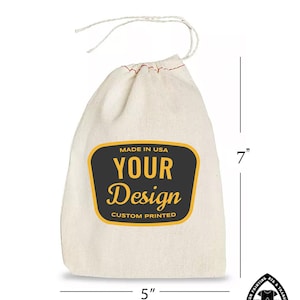 Op de afbeelding: Een witte katoenen trekkoordtas met een zwart en geel label waarop staat "Made in USA, Your Design, Custom Printed". De tas is 17,8 cm hoog en 12,7 cm breed.