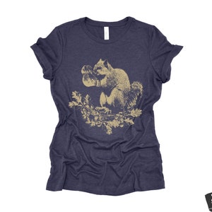 May include: A navy blue t-shirt with a vintage illustration of a squirrel holding a nut in its paws. The squirrel is surrounded by leaves and branches.