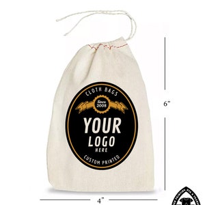 Op de afbeelding: Een witte katoenen trekkoordtas met een zwart en gouden logo met de tekst "Cloth Bags Since 2008 Your Logo Here Custom Printed". De tas is 15,2 cm hoog en 10,2 cm breed.