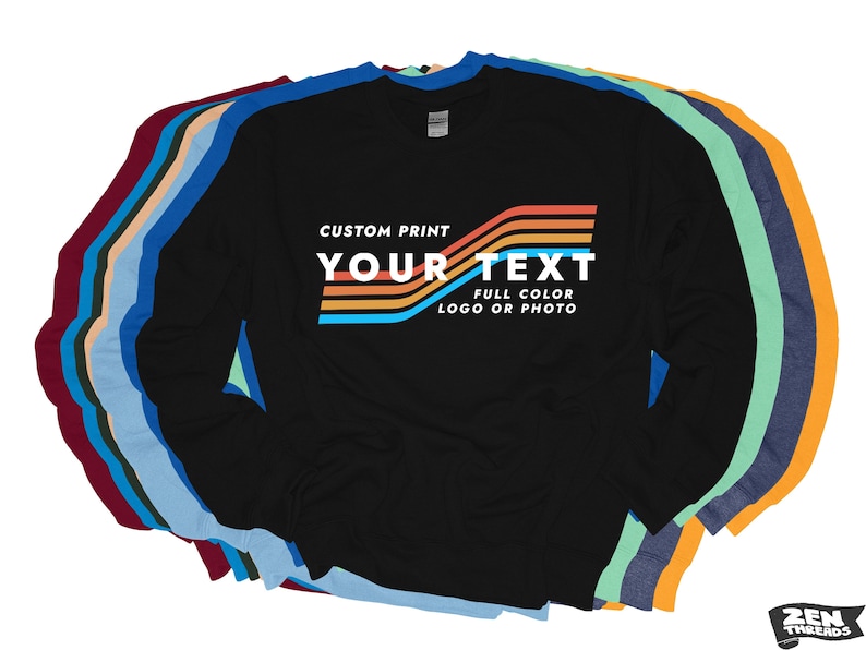 Puede incluir: Camiseta negra de manga larga con un dise&ntilde;o de impresi&oacute;n personalizado. El dise&ntilde;o presenta el texto "YOUR TEXT" en blanco, con rayas horizontales de colores arriba y abajo. La camiseta forma parte de una colecci&oacute;n de camisetas de manga larga de varios colores.