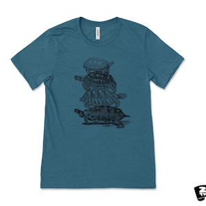 May include: Teal crew neck t-shirt with a black and white illustration of turtles stacked on top of each other. The shirt has short sleeves and a classic fit. The brand logo "Zen Threads" is in the bottom right corner.