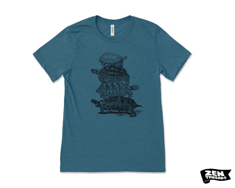 May include: Teal crew neck t-shirt with a black and white illustration of turtles stacked on top of each other. The shirt has short sleeves and a classic fit. The brand logo "Zen Threads" is in the bottom right corner.
