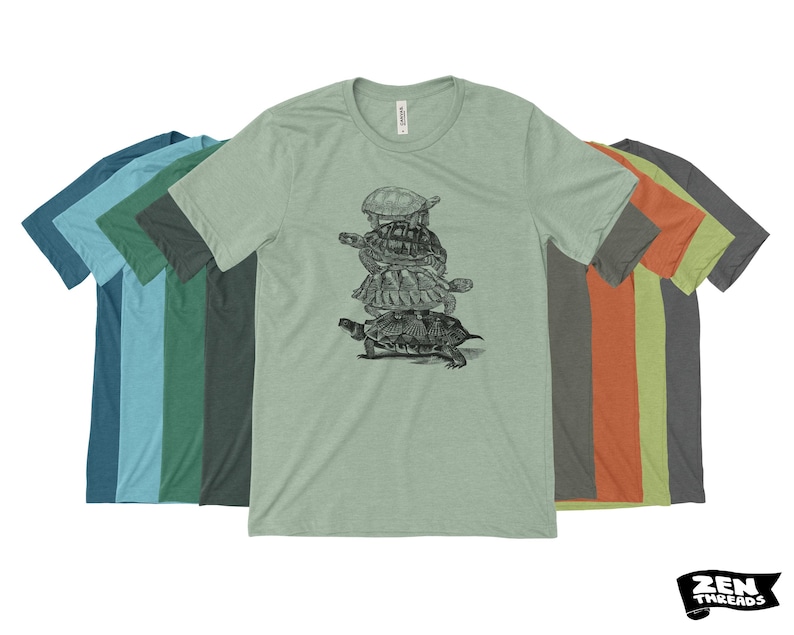 May include: A light green crew neck t-shirt with a black and white illustration of turtles piled up. Other t-shirts in shades of blue, green, and orange are visible. The Zen Threads logo is in the bottom right corner. The image shows a variety of colours.
