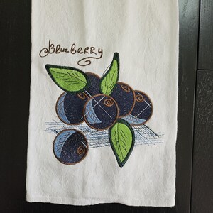 May include: White kitchen towel with embroidered blueberries and green leaves. The text "Blueberry" is embroidered in brown thread.