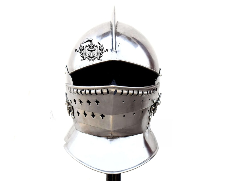 May include: A silver helmet with a visor and a crest on the top. The helmet has a decorative design around the visor and a small, pointed crest on top.