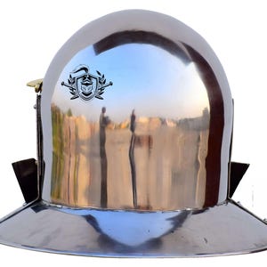 Pode incluir: Um capacete prateado com uma aba larga e uma crista no topo. O capacete &eacute; feito de metal e tem um acabamento brilhante.