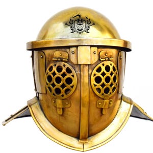 May include: A gold-colored gladiator helmet with a decorative design and a grill over the eyes. The helmet has a crest on top with a shield and swords.