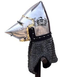 May include: A silver helmet with a pointed visor and a chainmail coif. The helmet has a gold trim and a crest on the top.