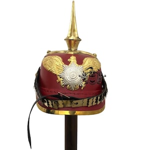 May include: A red leather Prussian Pickelhaube helmet with a gold eagle and a brass spike on top. The helmet has a black leather chin strap and a gold trim around the base.