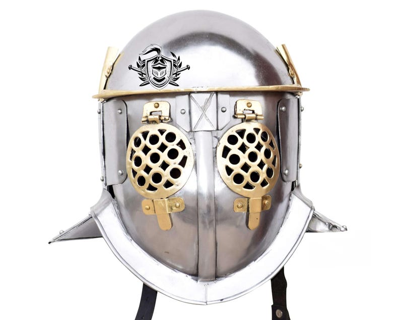 Pode incluir: Um capacete de gladiador prateado com guarni&ccedil;&atilde;o de lat&atilde;o e uma grelha de lat&atilde;o sobre os olhos. O capacete tem uma crista com um cavaleiro e uma espada.