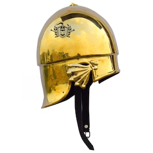 May include: A gold helmet with a black crest and a leather strap. The helmet has a decorative design on the side.