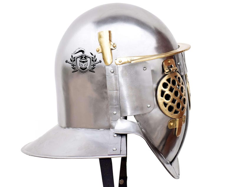 Pode incluir: Um capacete de prata com uma viseira de lat&atilde;o e uma crista decorativa no lado. O capacete tem uma m&aacute;scara facial de malha e uma correia de couro.