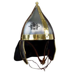 May include: A silver and brass helmet with a pointed top and a leather flap on the back. The helmet has a decorative design on the front.