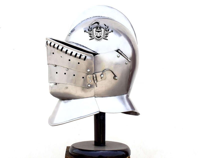 May include: A silver knight's helmet with a visor and a crest on the top. The helmet is on a black stand.