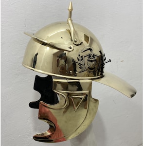 May include: A gold Roman helmet with a crest and a visor. The helmet has a decorative design on the side.