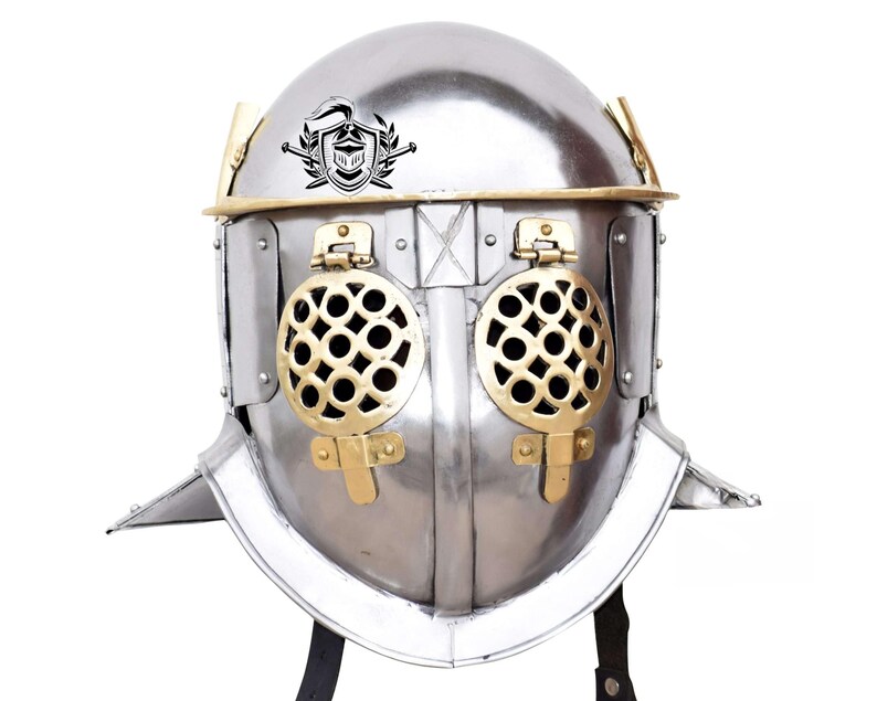 Pode incluir: Um capacete de gladiador prateado com guarni&ccedil;&atilde;o de lat&atilde;o e uma grelha de lat&atilde;o sobre os olhos. O capacete tem uma crista com um cavaleiro e uma espada.