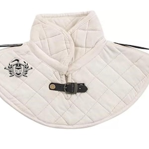 May include: White quilted fabric neck guard with a black leather buckle and a black embroidered emblem of a knight's helmet, shield, and crossed swords.