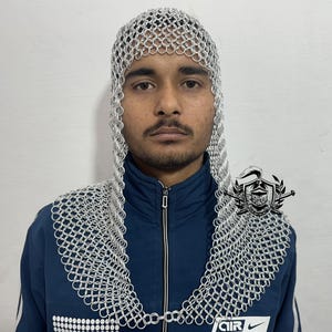 Puede incluir: Una capucha de cota de malla plateada con una punta puntiaguda. La capucha está hecha de anillos de metal entrelazados y cubre la cabeza y el cuello.